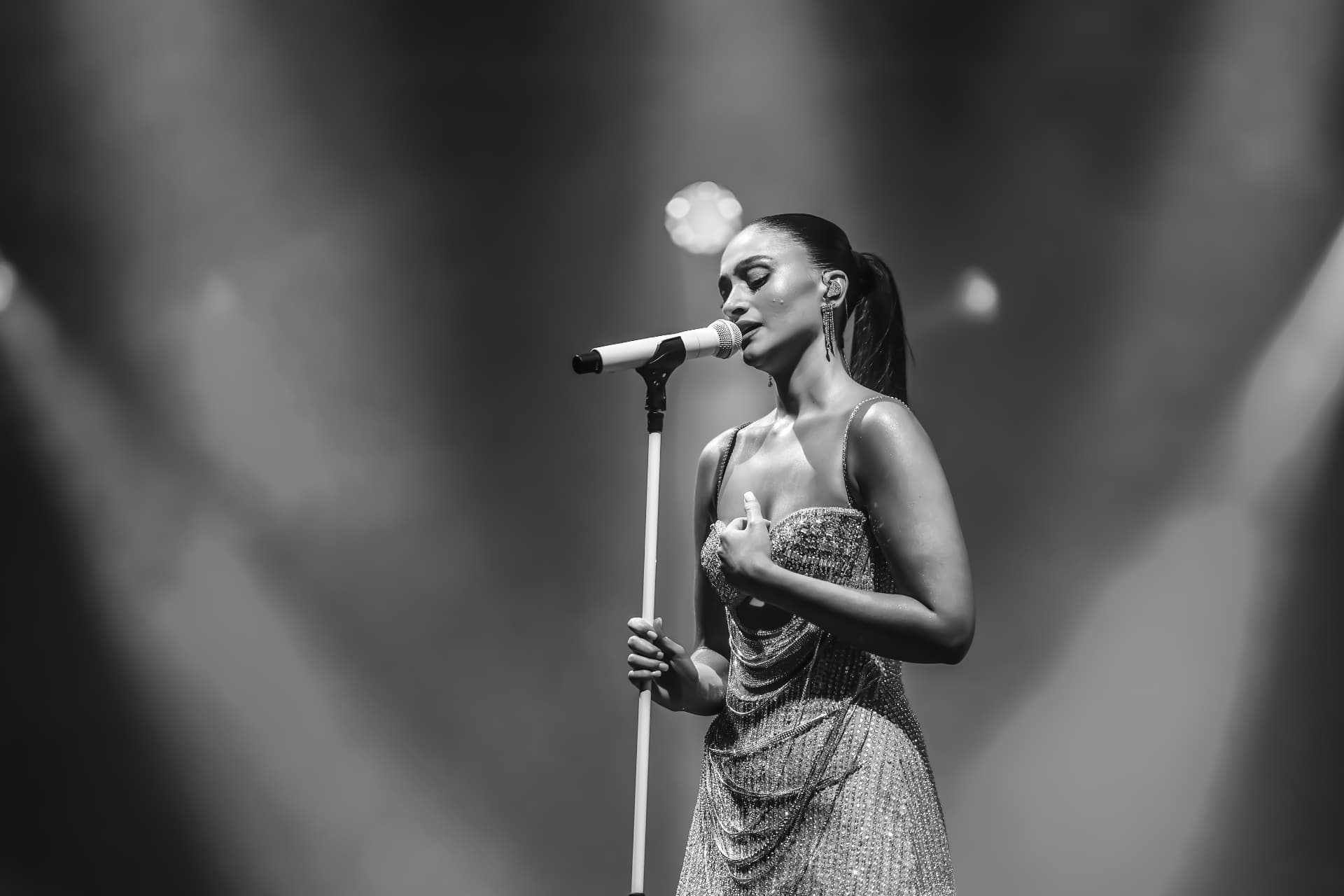 Agam Buhbut in black and white, singing at the microphone stand